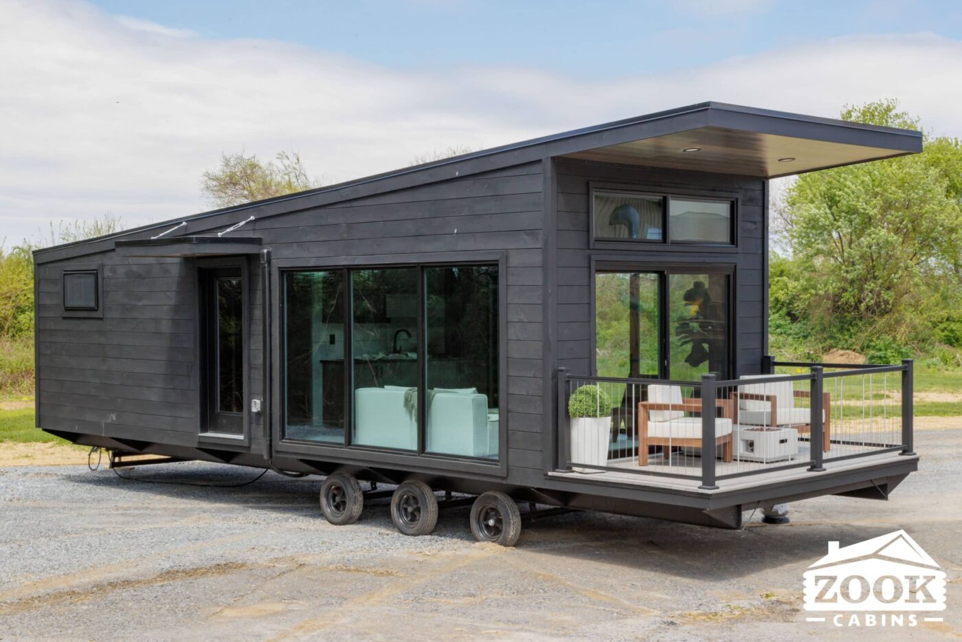 Modern black Rockwood park model tiny home on wheels with large glass doors, full windows, and a small front porch with outdoor seating.