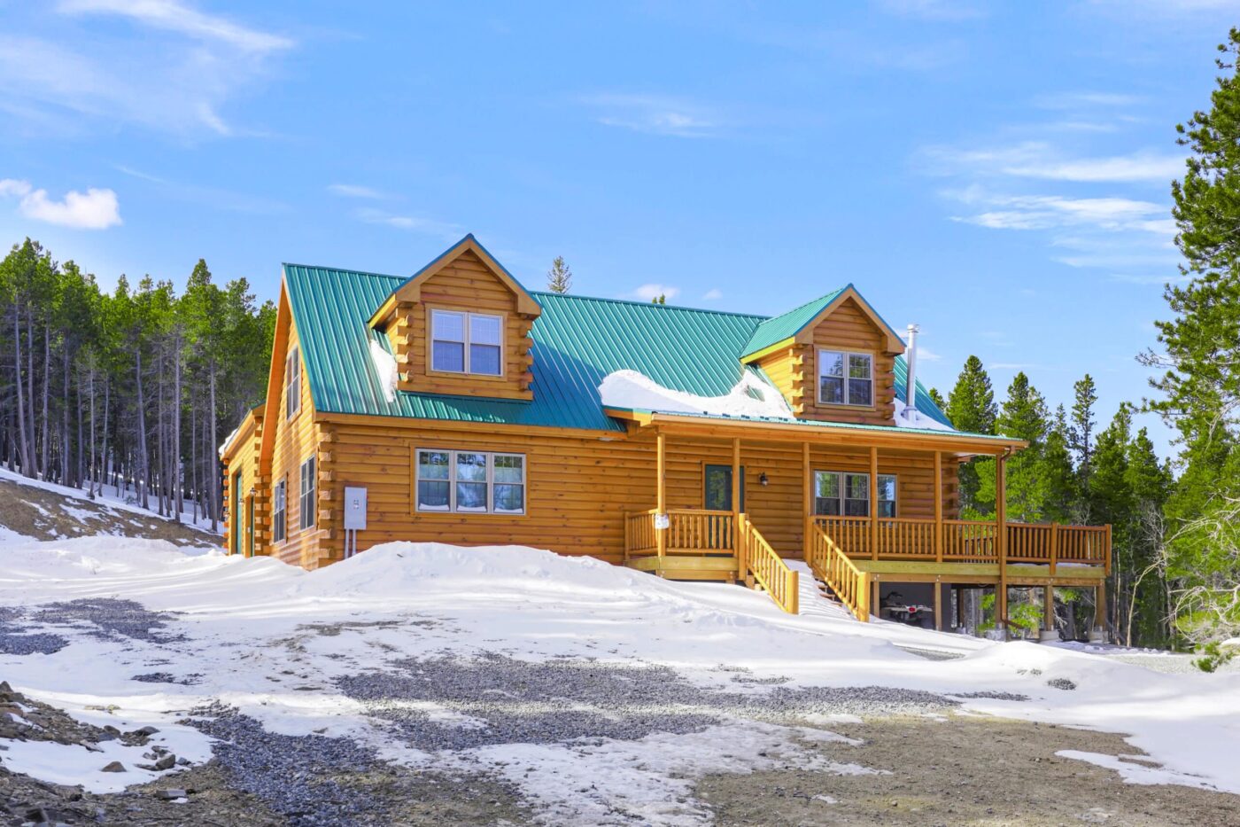 Two-story log cabin with green roof surrounded by snow and evergreens in West Virginia.