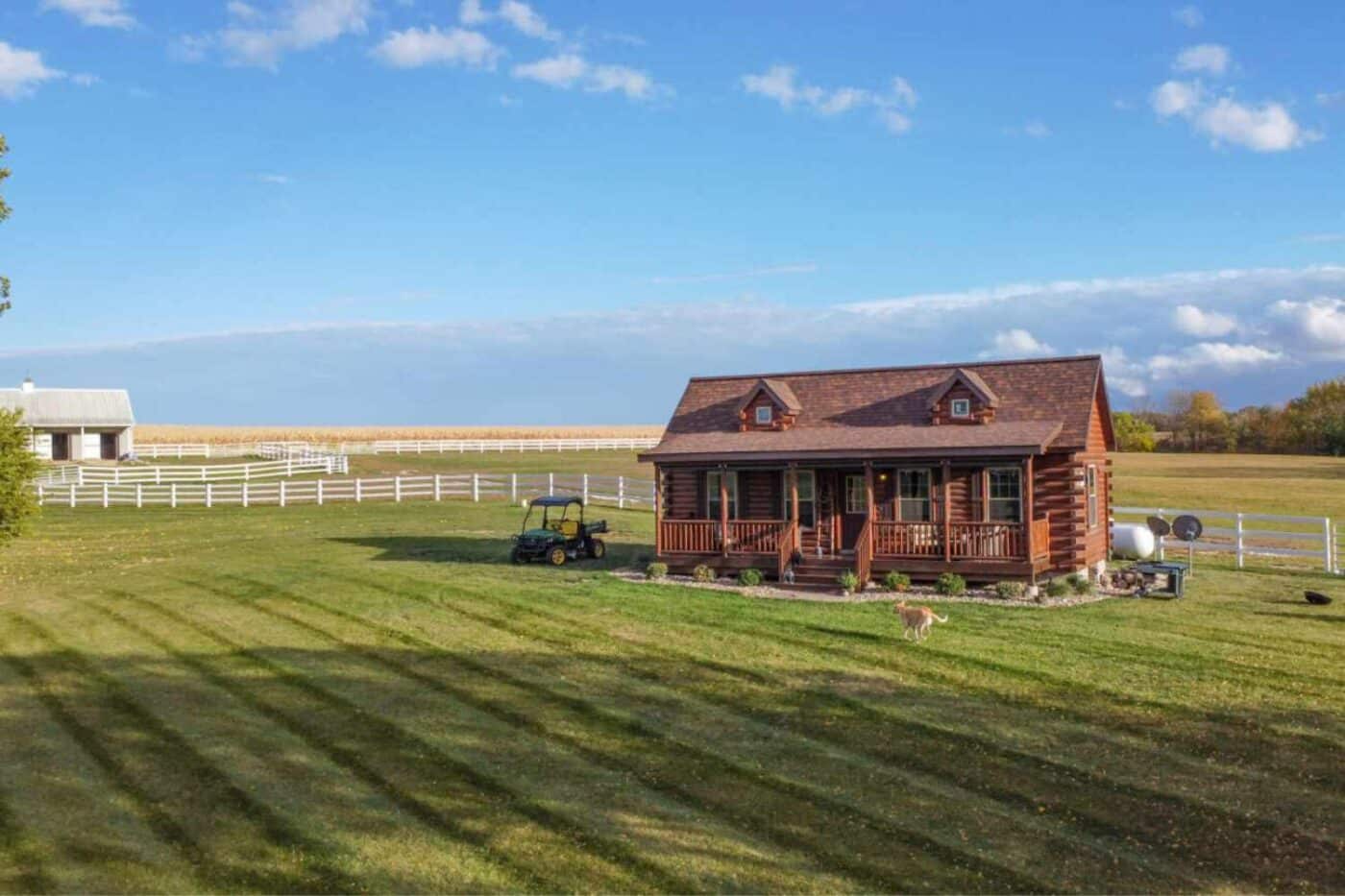 Log cabin on farm with dog running through front yard and tractor golf cart to side of cabin