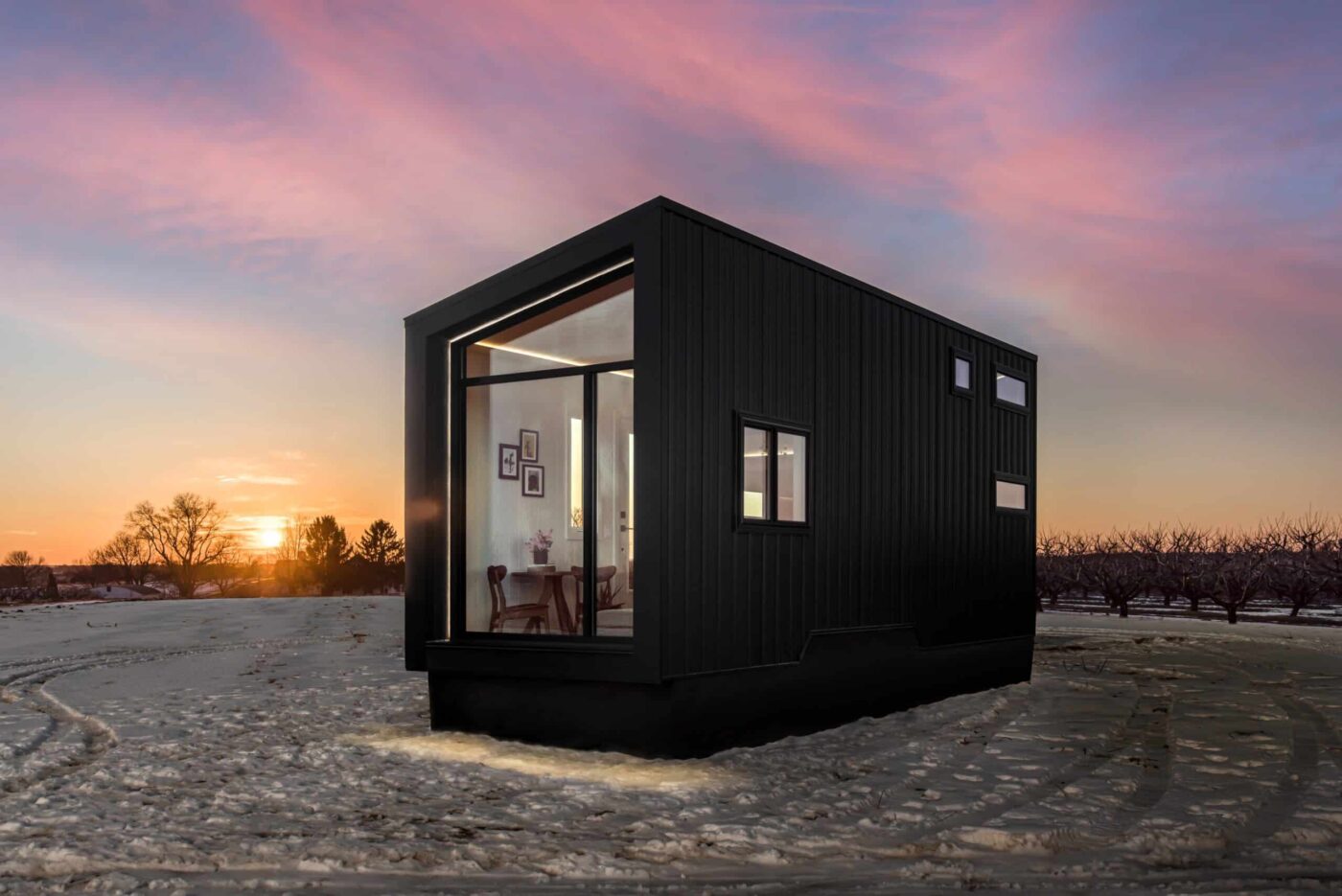 Modern black Luna park model tiny home with large windows, set against a sunset backdrop.
