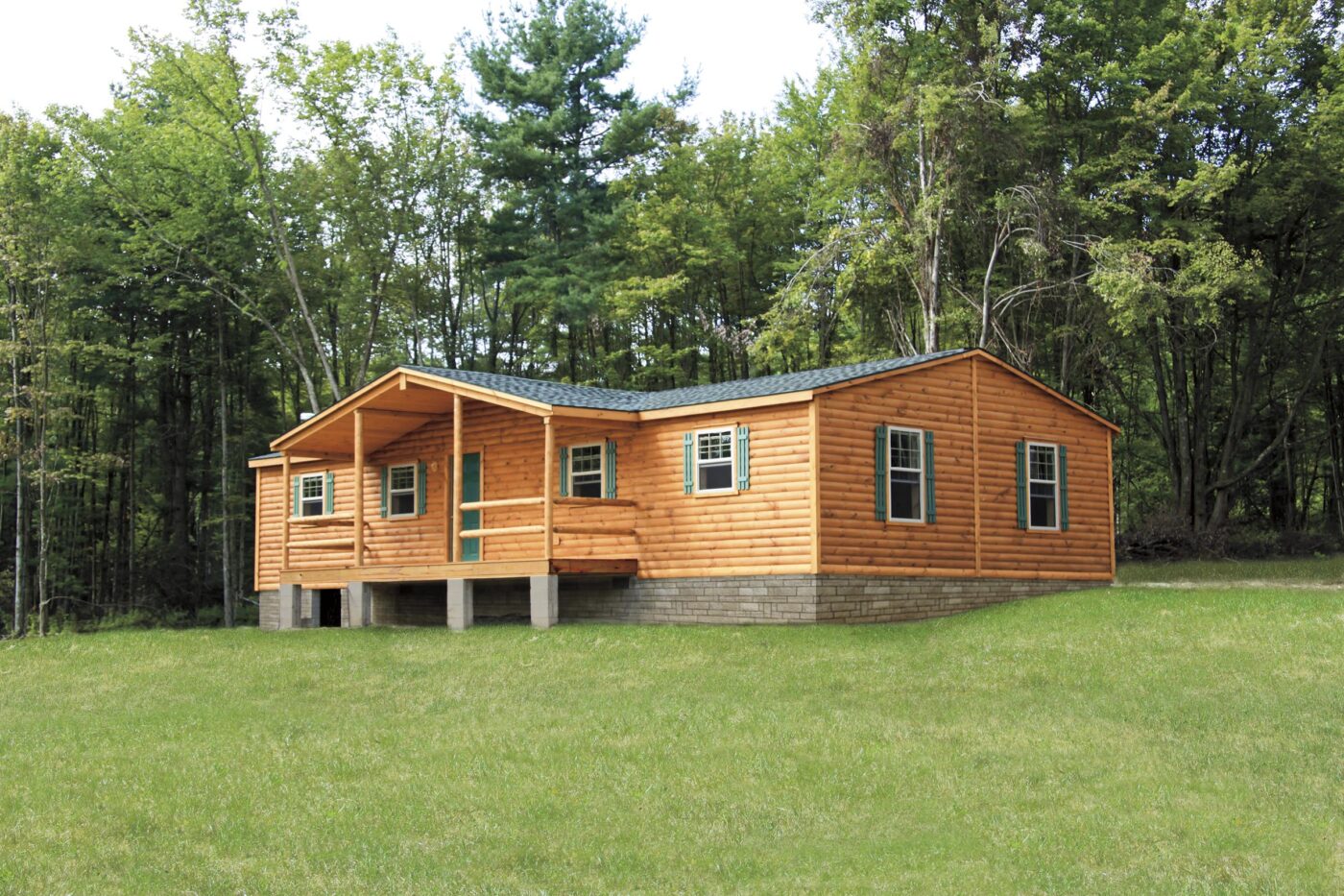 Single-story Pioneer log cabin on a raised foundation, with green shutters and a covered porch.