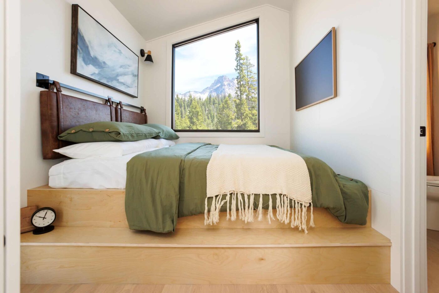 Cozy bedroom in an A-frame park model tiny home with a mountain view through a large window.