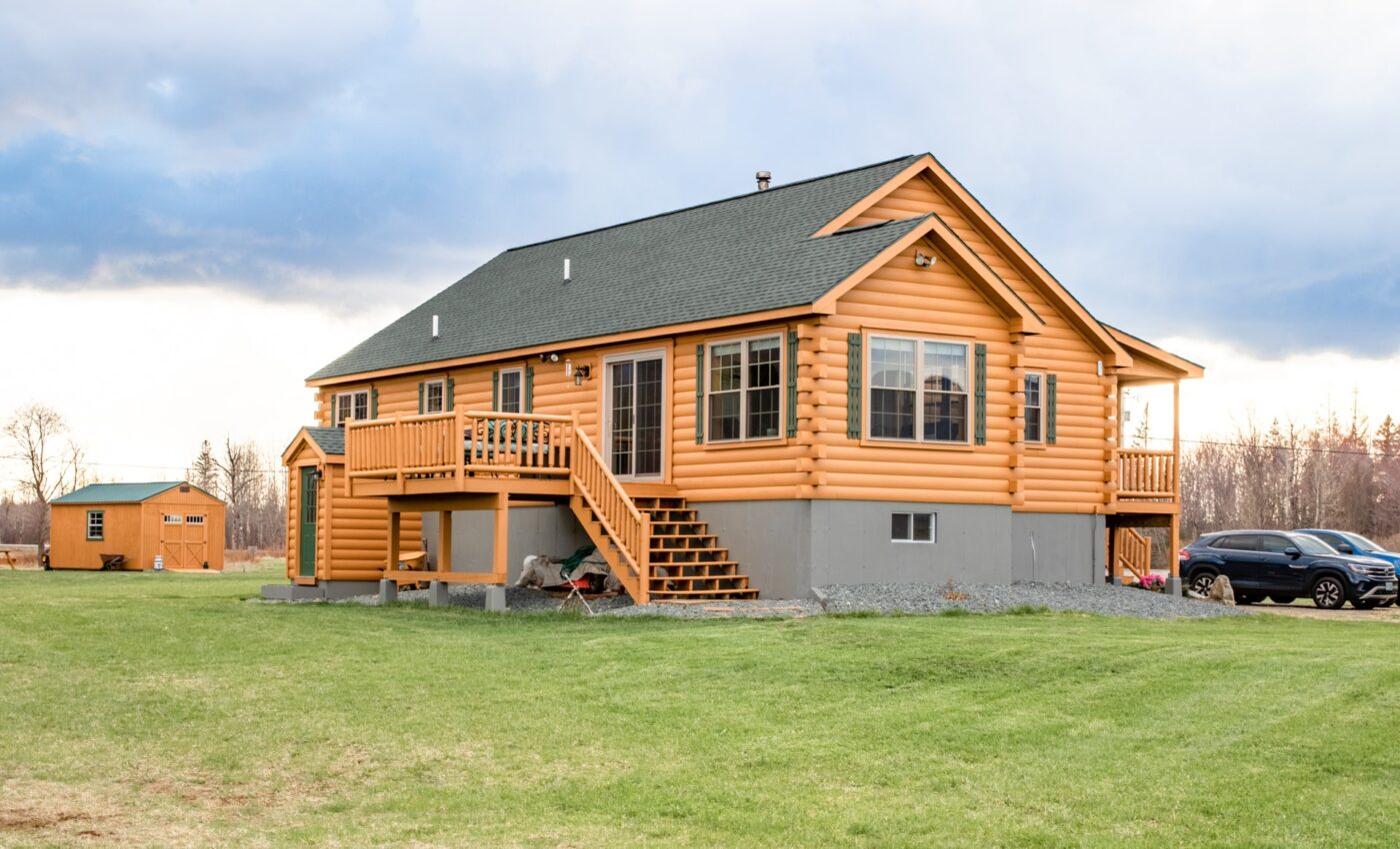 Medium-sized log cabin with covered front porch, elevated foundation, and a sloped gravel driveway.