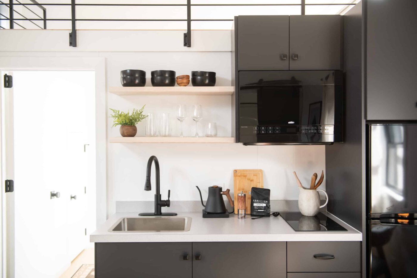 Modern tiny home kitchen with black cabinetry, built-in microwave, and open shelving.