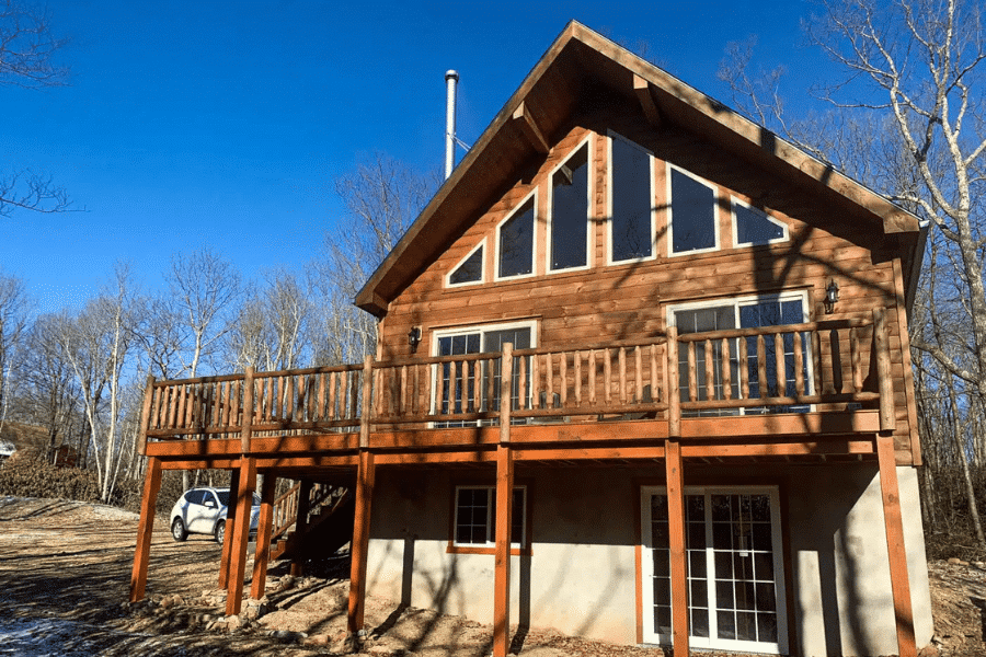 Chalet-style log cabin with tall windows and raised deck in Rhode Island.