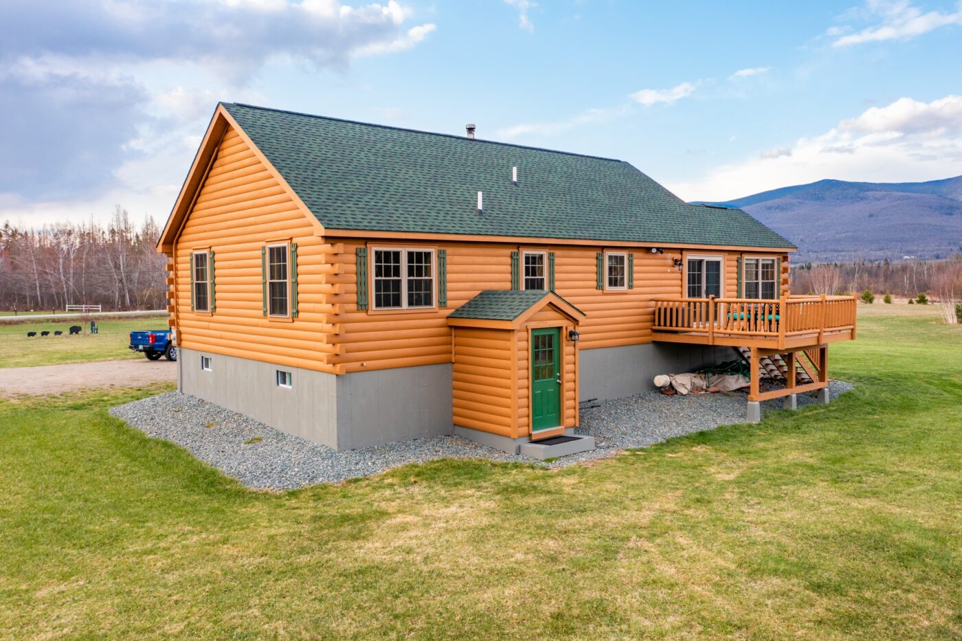 Log cabin with green roof and walkout basement set against open grassland and mountain views.