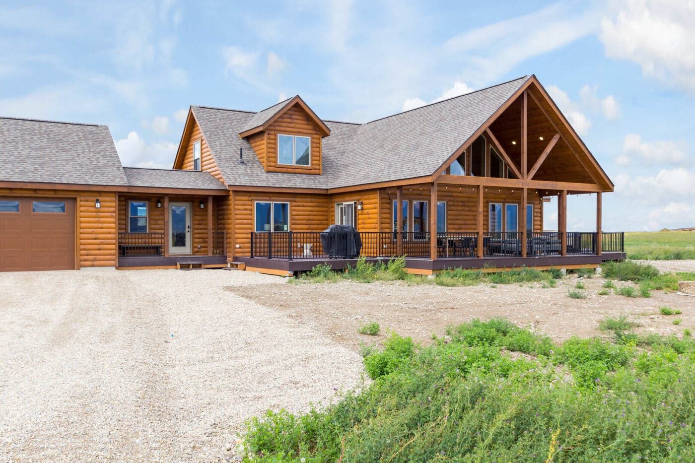 Large two-story log cabin with covered porch, attached garage, and wide windows under a clear sky.