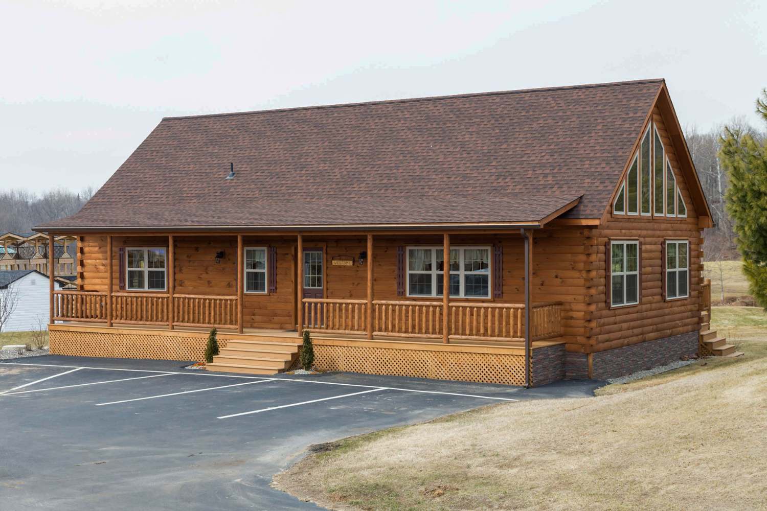 Log cabin on foundation in front of parking lot with porch and windows